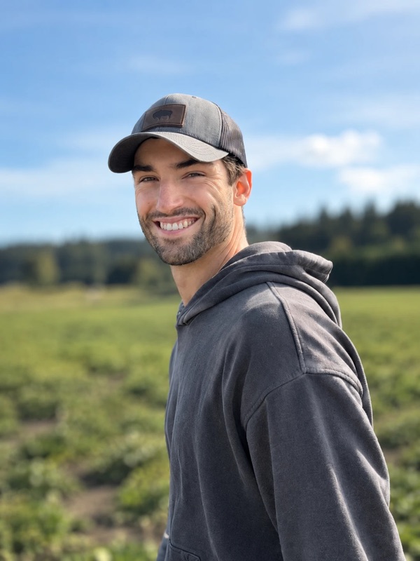 Cormac McIntosh, founder of Breakwater Sauna, smiling outdoors in a cap and hoodie